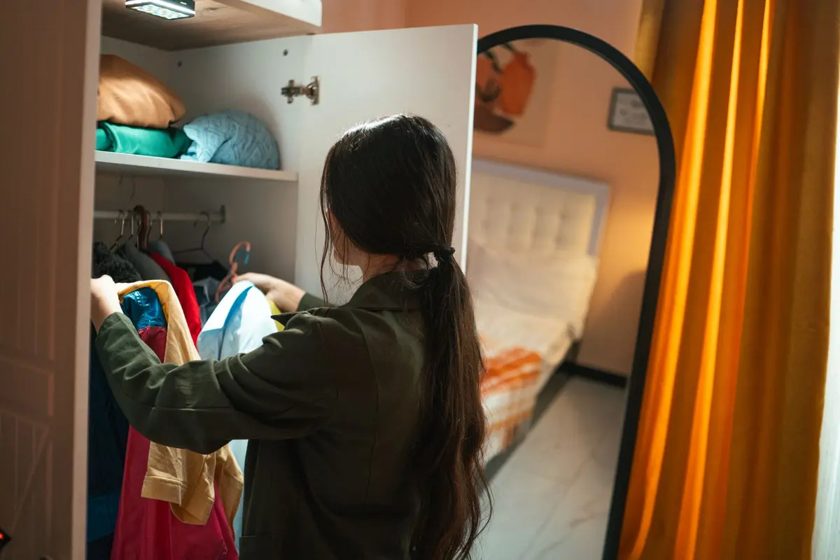 Woman choosing clothes from an open bedroom closet with shelves and a hanging rail